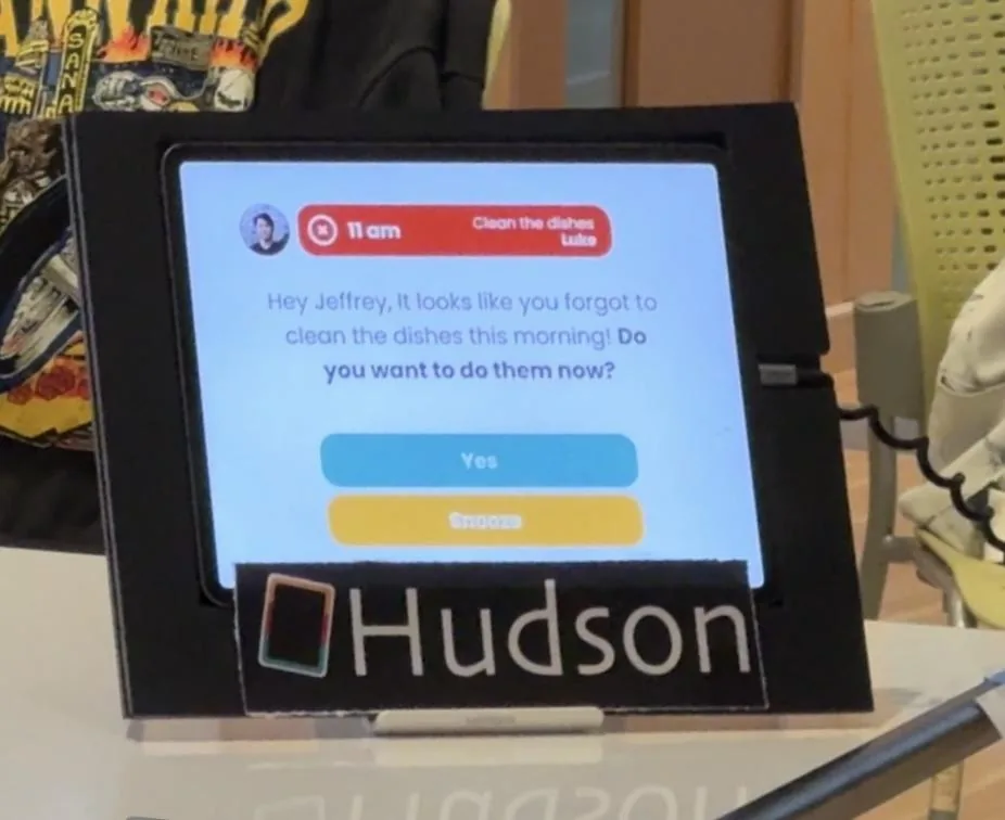 Photo of the Hudson hub prototype, an iPad in a black frame with the Hudson logo, showing a reminder asking Jeffrey if he wants to clean the dishes now, with Yes and Snooze buttons.